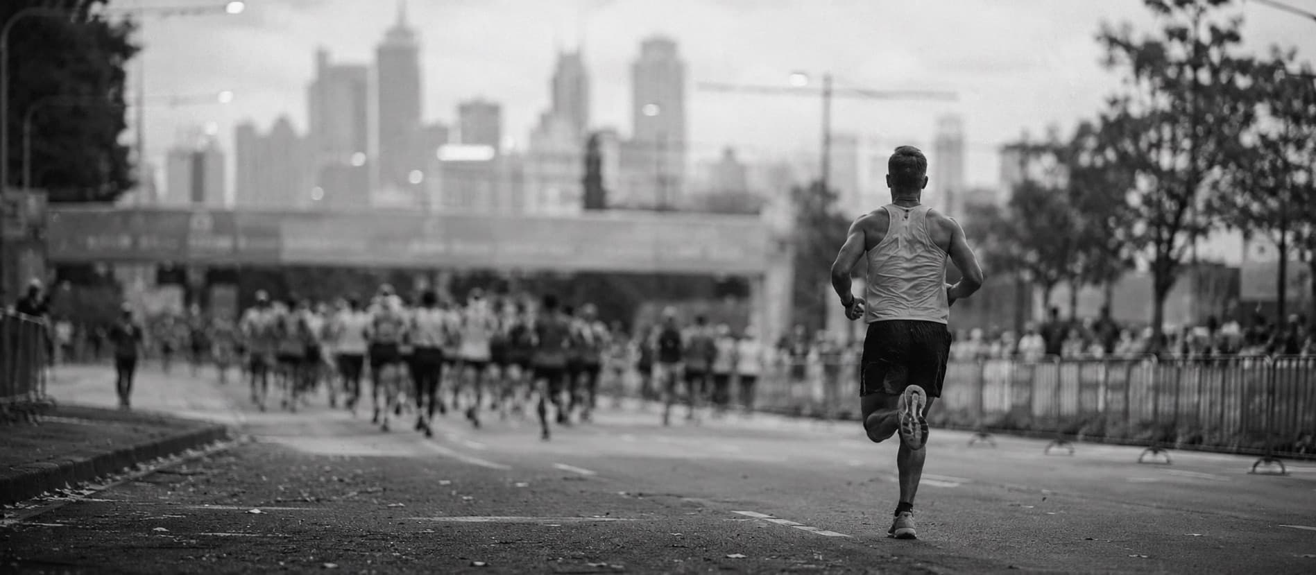 A runner on the road into the city, mid-race, with the field behind